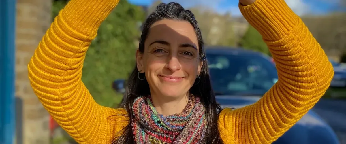 Helen in a vibrant yellow jumper, smiling and shading her eyes from the sun