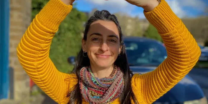 Helen in a vibrant yellow jumper, smiling and shading her eyes from the sun
