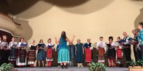 Helen conducts a Bulgarian choir wearing traditional dress, and Zarebi members
