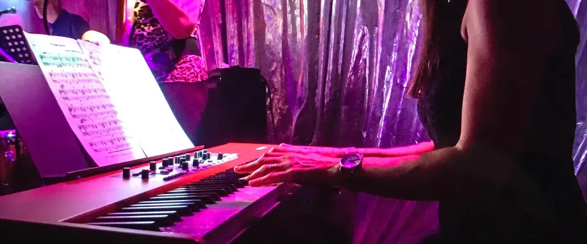 Close up photo of Helen sitting at her Nord stage piano, performing with band